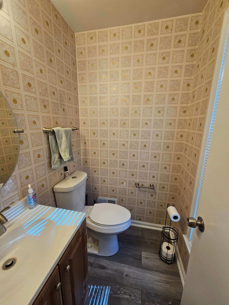 Before picture of our half bathroom. It had wallpaper from the 1970s and grey vinyl planking.