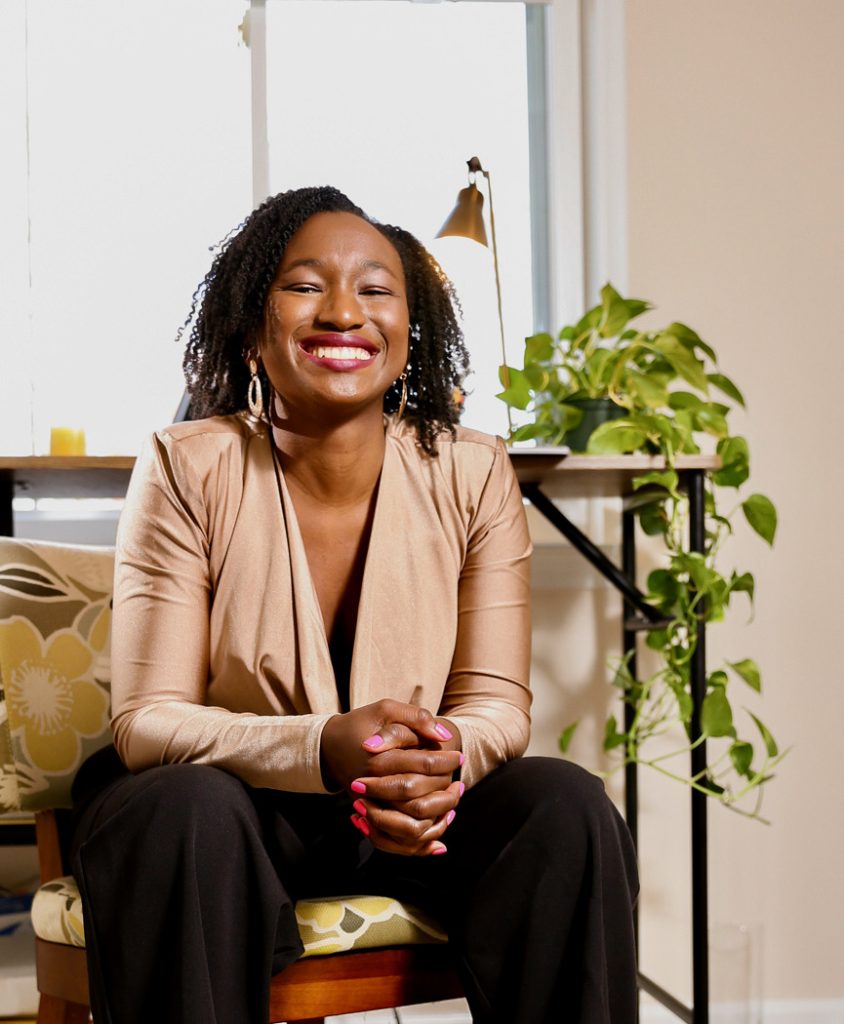 Picture of Jamie smiling and sitting in a chair with her arms rested on her legs